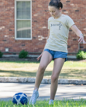 Girl with an Olympia Girl t-shirt kicking a soccer ball