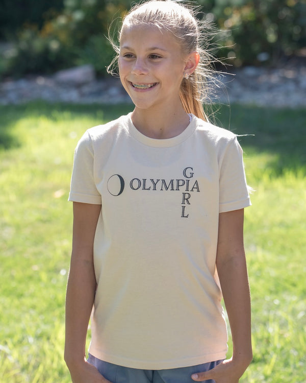 Young girl wearing a 'Olympia Girl' t-shirt outdoors on a sunny day.