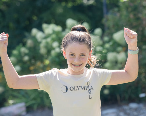 Girl wearing a 'Girl Olympia' t-shirt with arms raised outdoors.