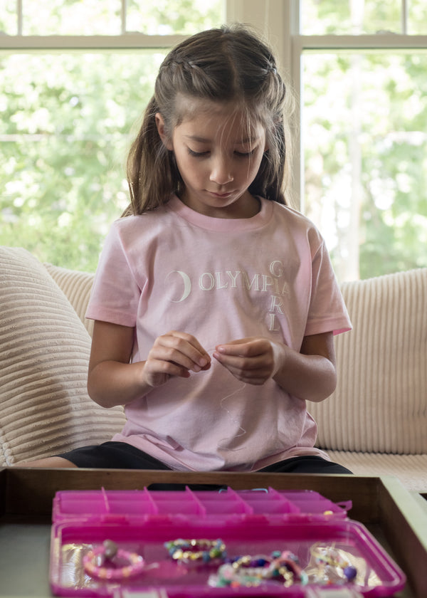Young girl sitting on a couch with a pink jewelry box and beads.